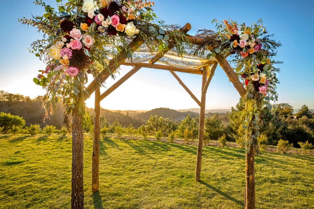 Outdoor chuppah with flowers on the top in sunshine.